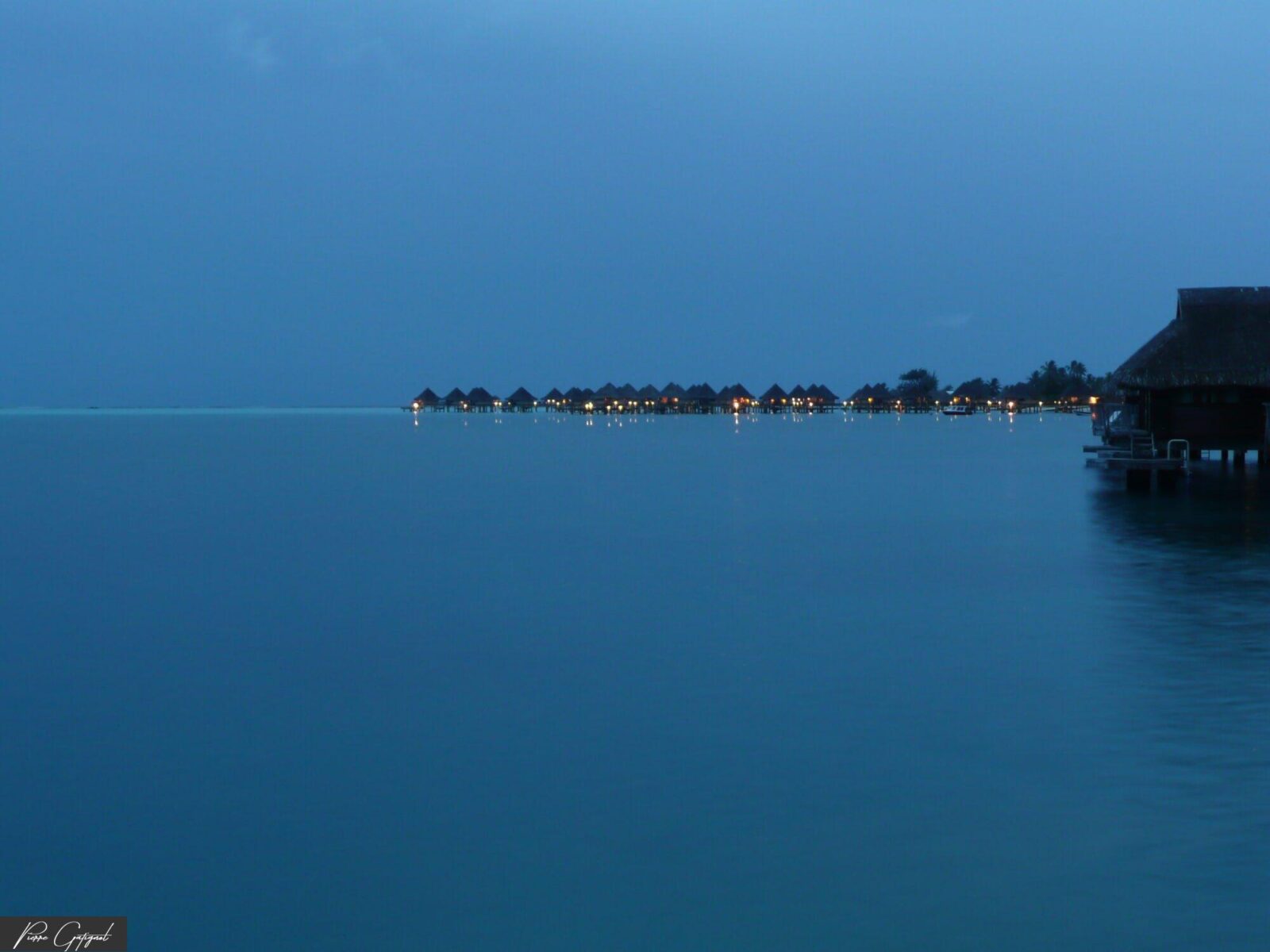 Lagon bleu au crépuscule avec bungalows sur pilotis éclairés