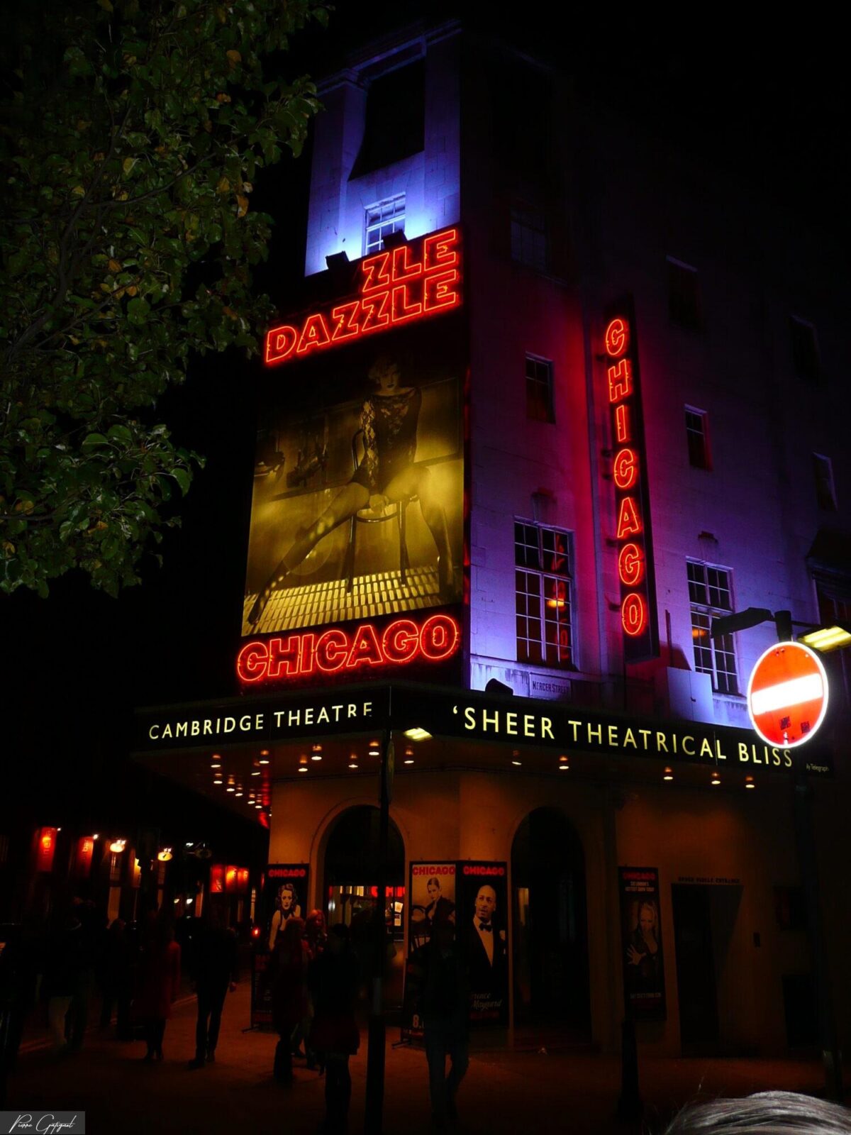 Façade nocturne du Cambridge Theatre éclairée par des enseignes