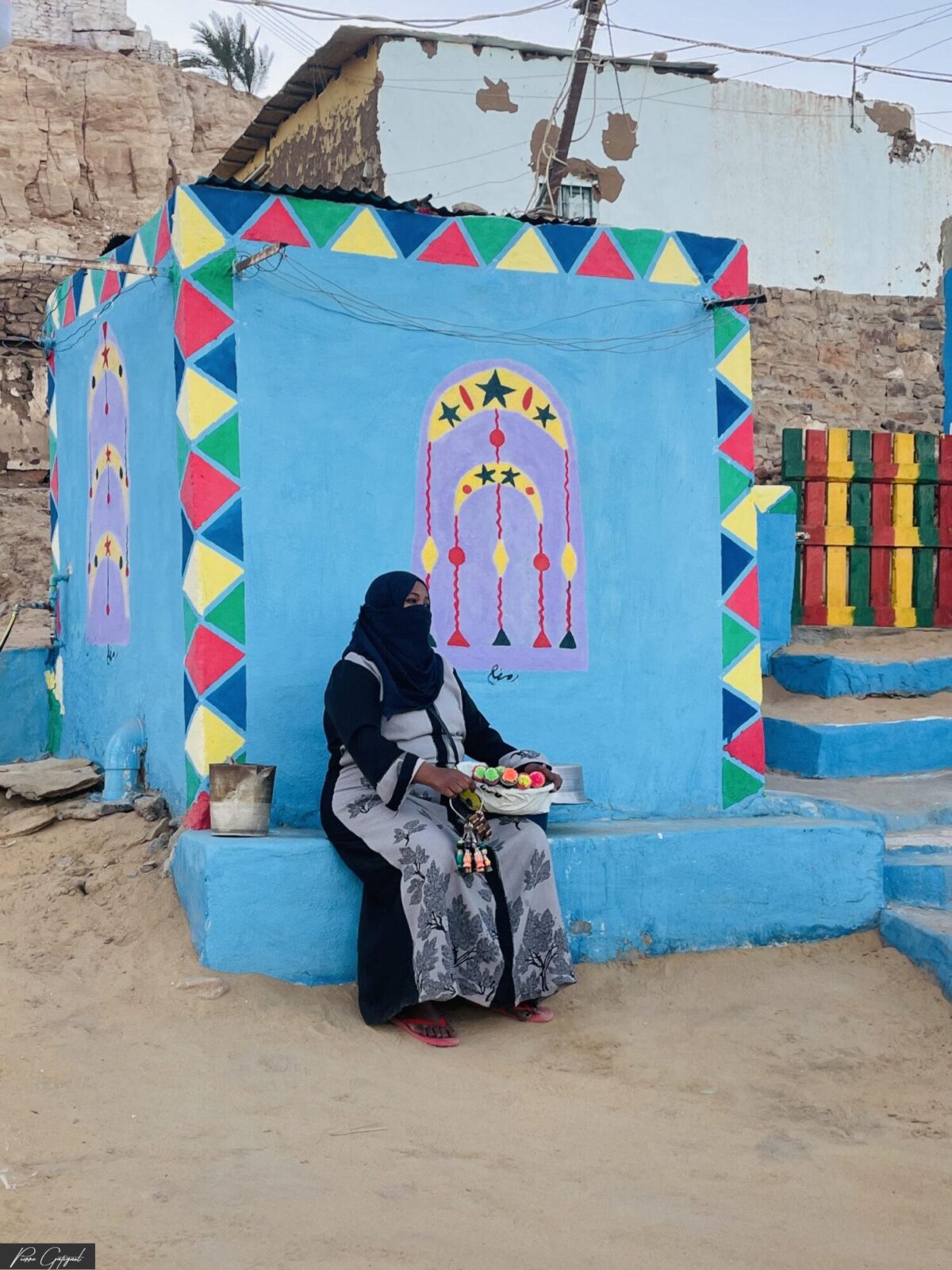 Femme assise devant une façade bleue décorée de motifs colorés