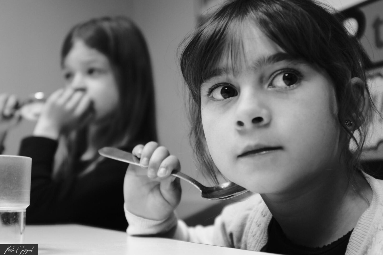 Deux enfants à table, l’une tenant une cuillère