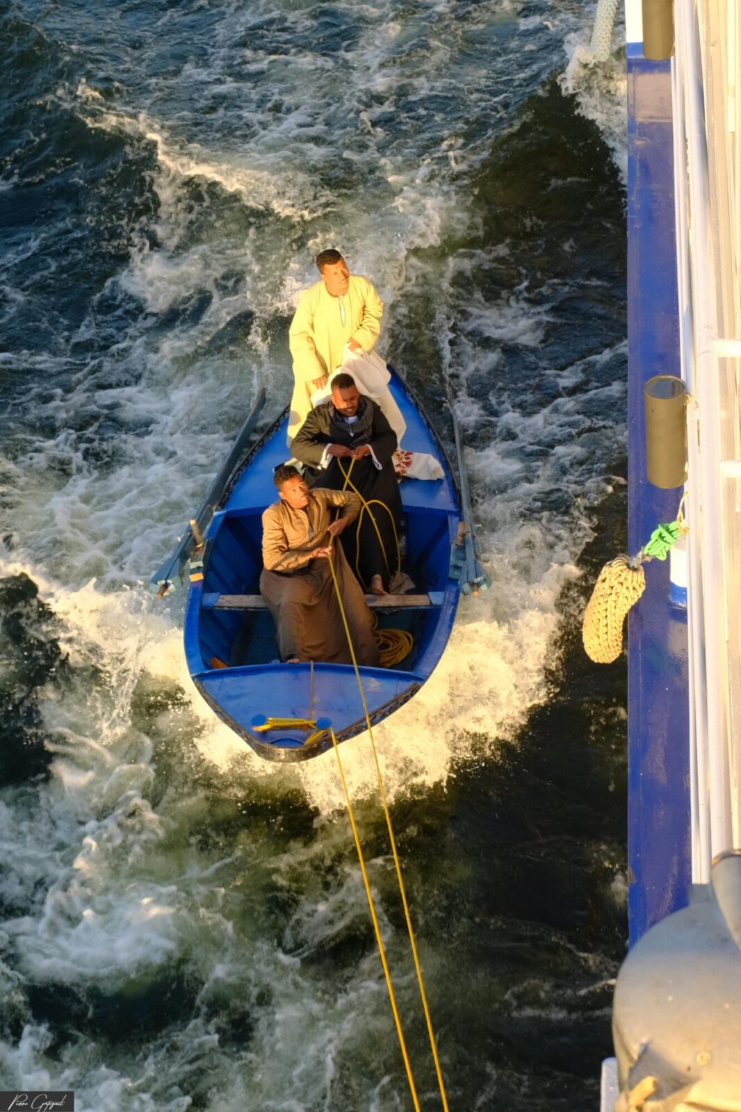 Trois marins dans une barque bleue sur une mer agitée
