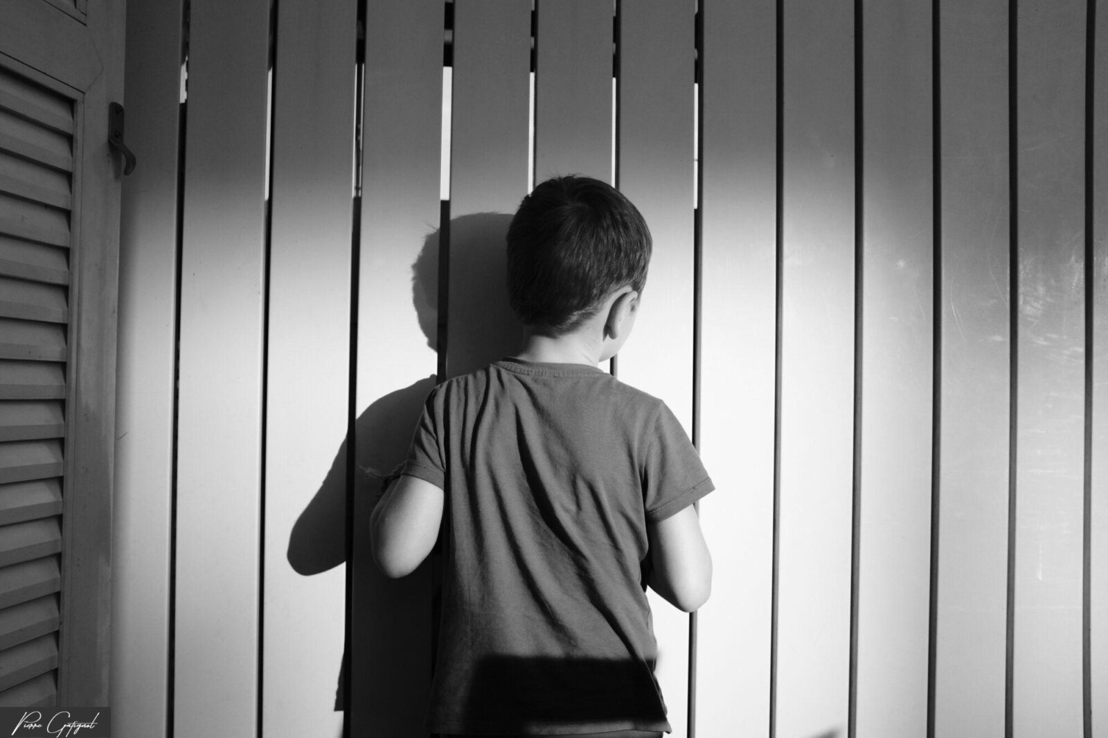 Enfant de dos devant des stores verticaux et son ombre