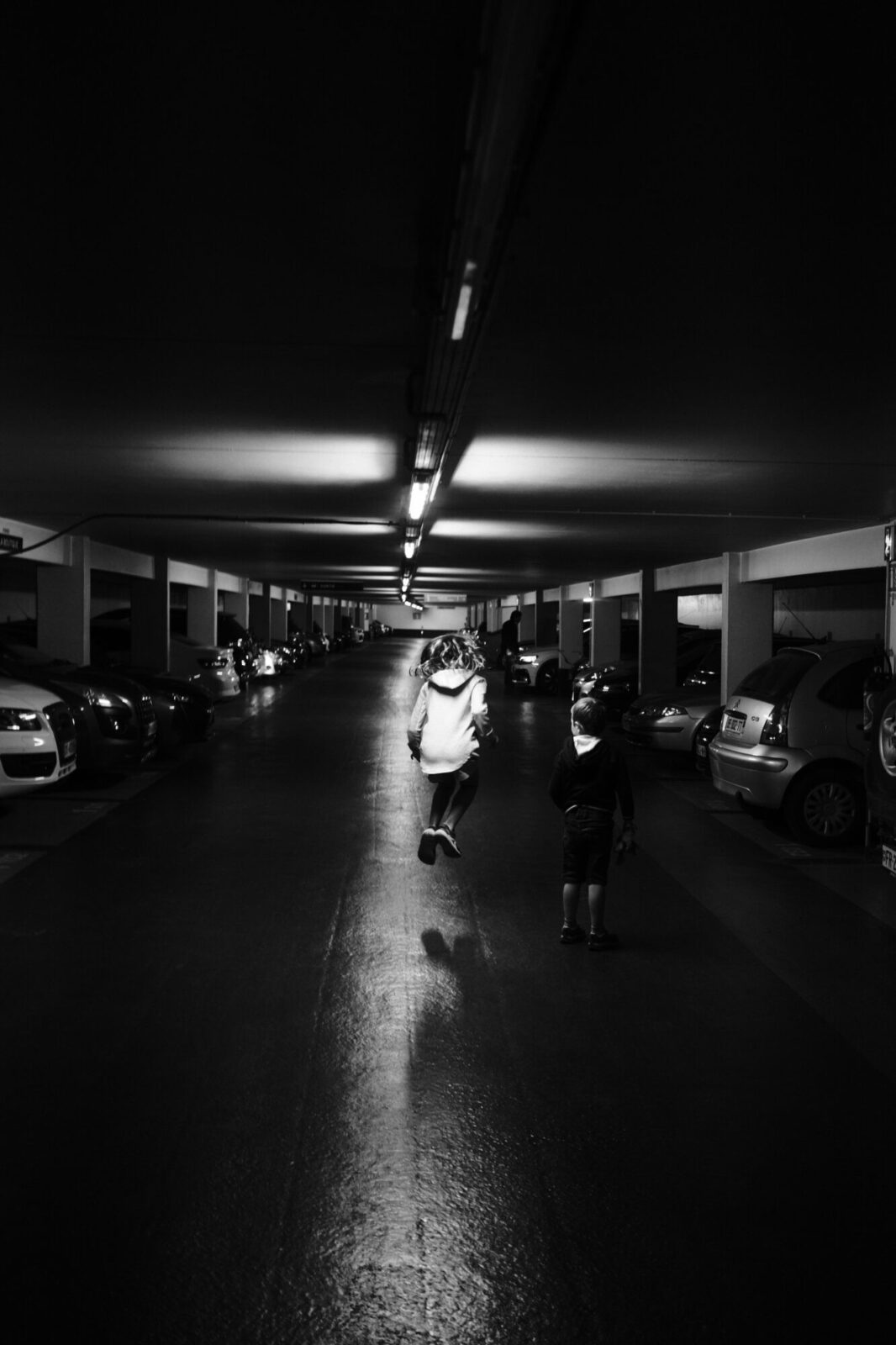 Deux personnes marchant entre des voitures dans un parking couvert