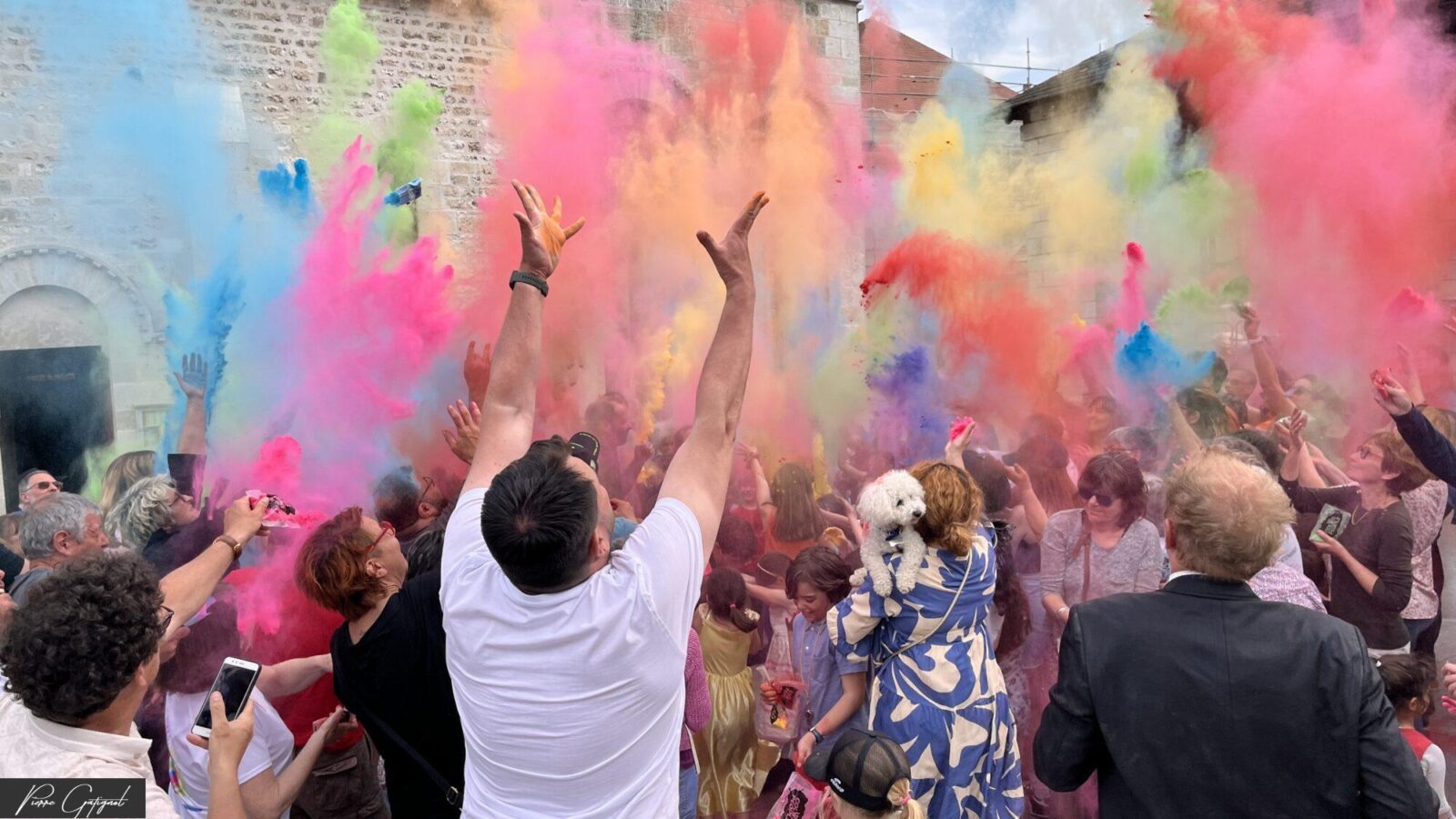 Foule lançant des poudres colorées devant un bâtiment en pierre.