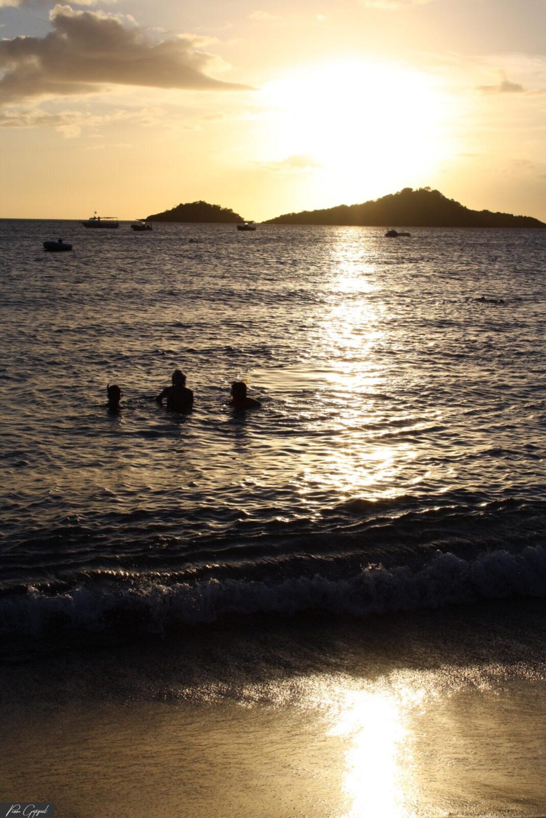 Baigneurs dans la mer au coucher de soleil devant des îlots