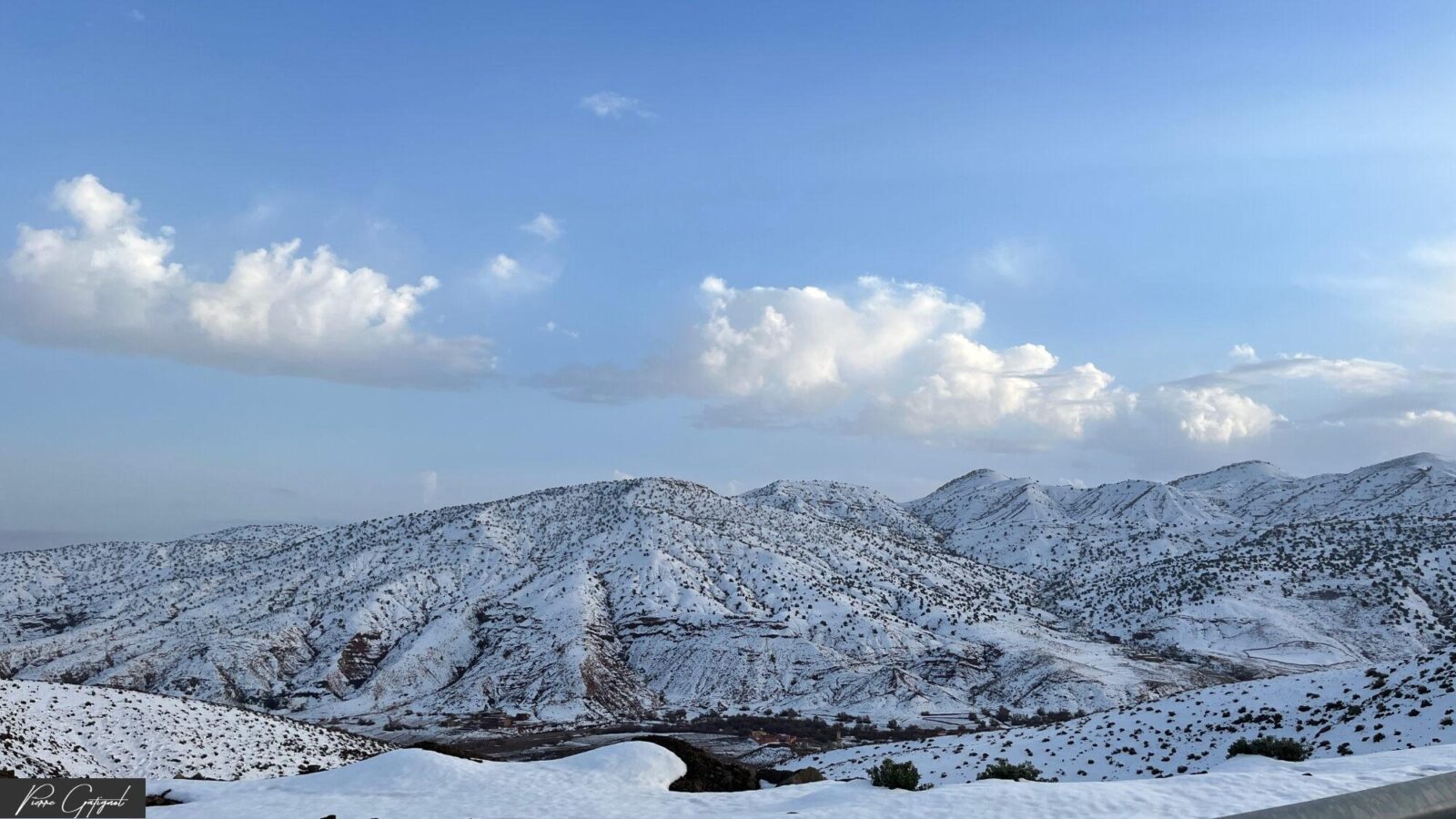 Collines montagneuses enneigées sous un ciel bleu nuageux