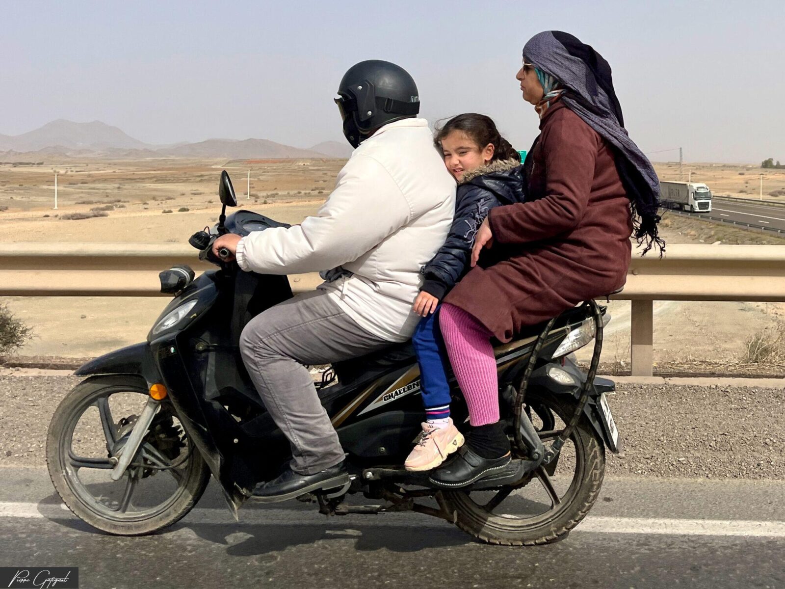 Trois personnes sur une moto le long d’une route désertique