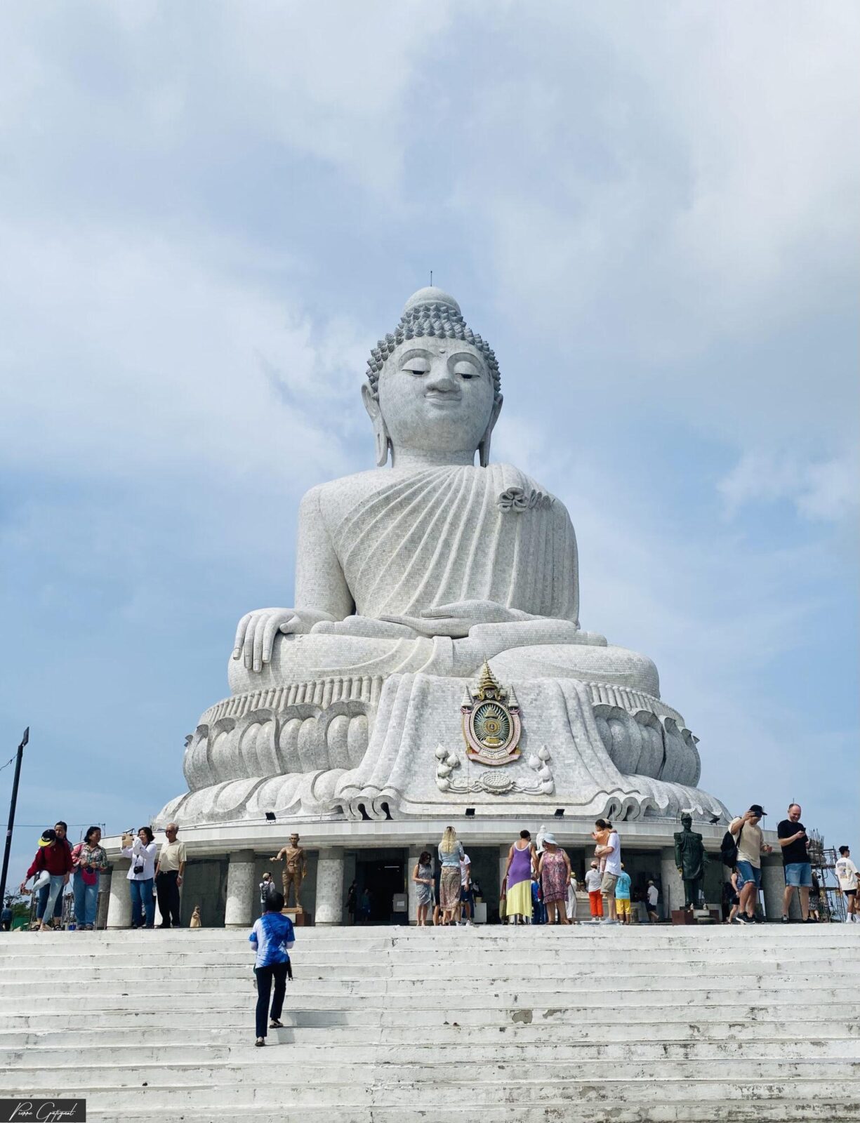 Grande statue blanche de Bouddha devant des visiteurs sur des marches