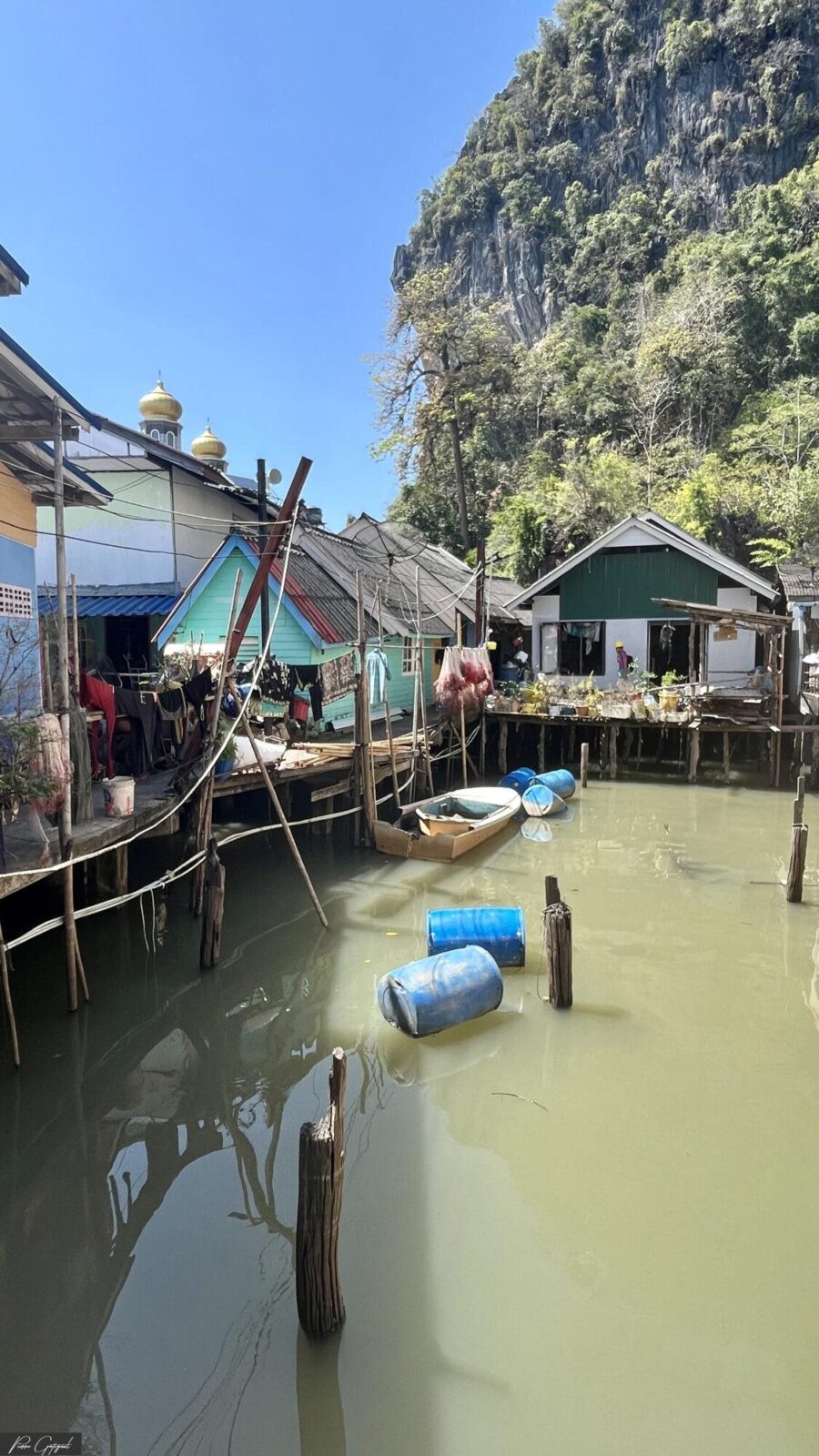 Maisons sur pilotis le long d’un canal au pied d’une falaise