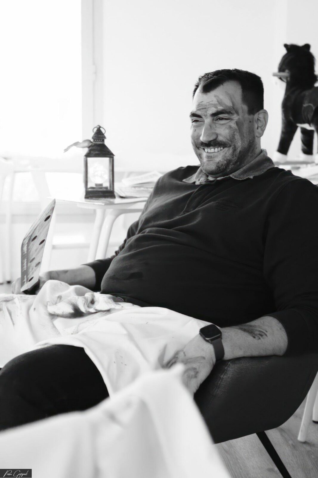 Homme souriant assis dans un fauteuil, tenant un journal