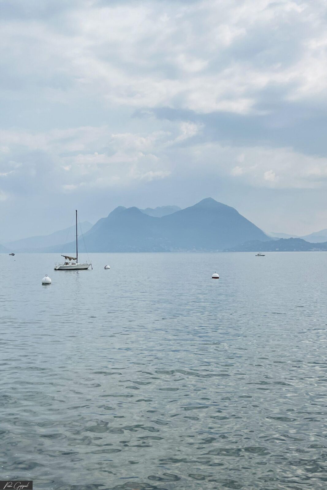 Voilier et bouées sur un lac devant des montagnes brumeuses