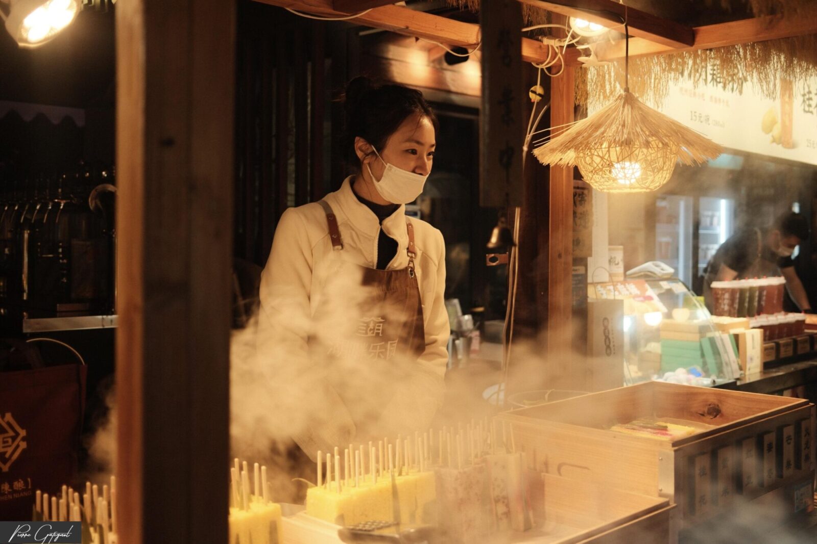 Vendeuse masquée derrière un comptoir avec vapeur et brochettes