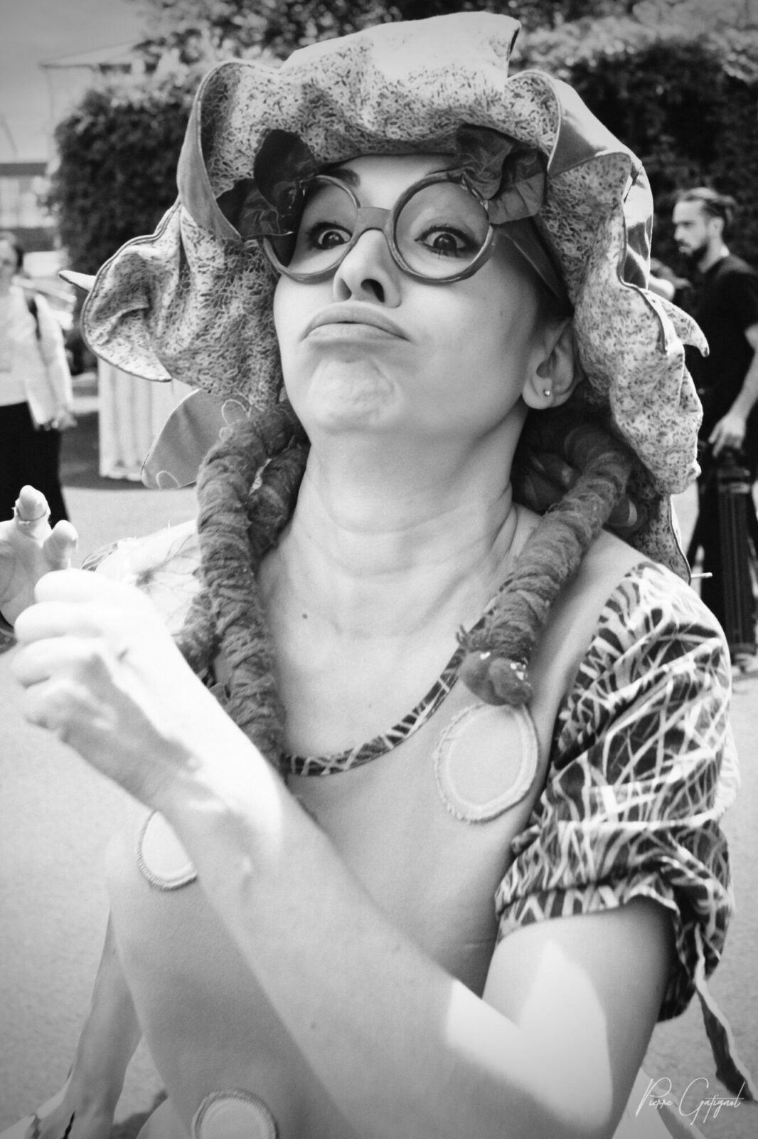 Femme portant un grand chapeau et des lunettes, faisant une grimace.