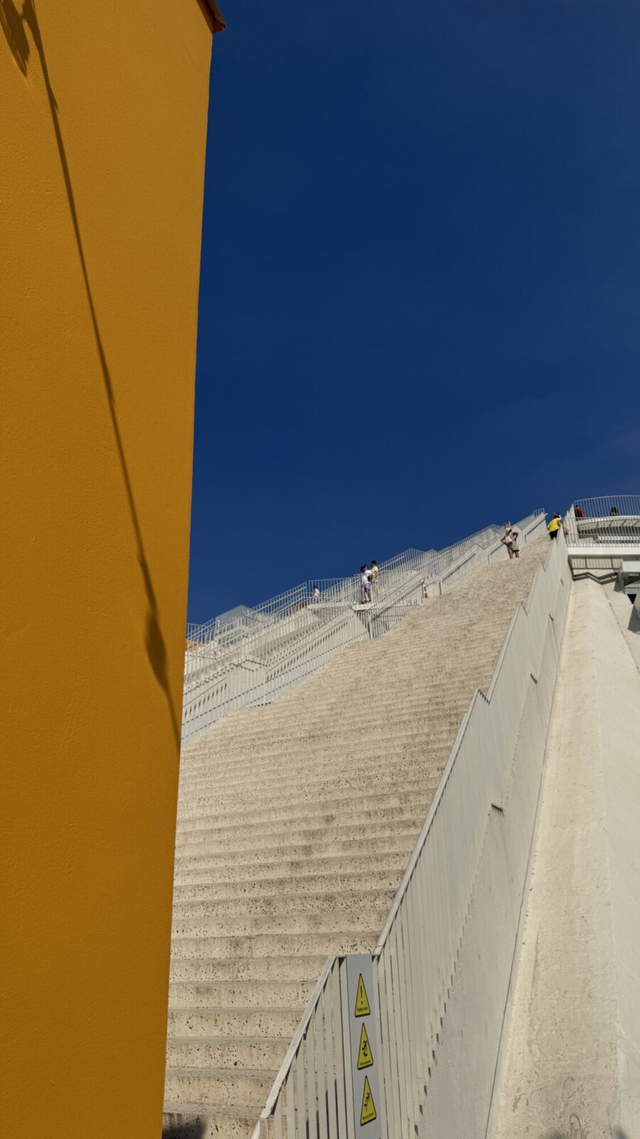 Escalier monumental vu depuis le bas, encadré par un mur jaune